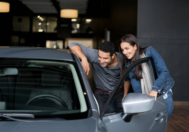 pareja mirando un coche para comprar en el concesionario - new automobile fotografías e imágenes de stock