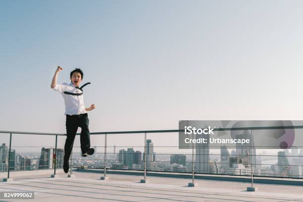 Young Handsome Asian Businessman Jumping High Celebrate Success Winning Pose On Building Rooftop Work Job Or Successful Business Concept Cityscape Background With Copy Space On Sunny Blue Sky Stock Photo - Download Image Now