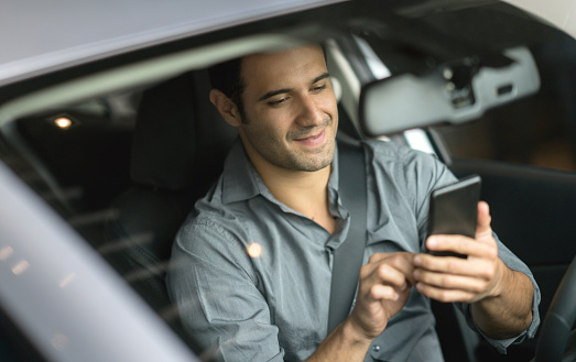 Portrait of a Latin American man using his cell phone while driving a car â lifestyle concepts