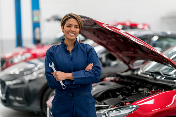 Portrait of a female mechanic looking at camera as her colleague works in the background.