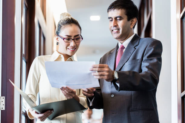 istock Executive and secretary standing in office hallway discussing papers 825005742