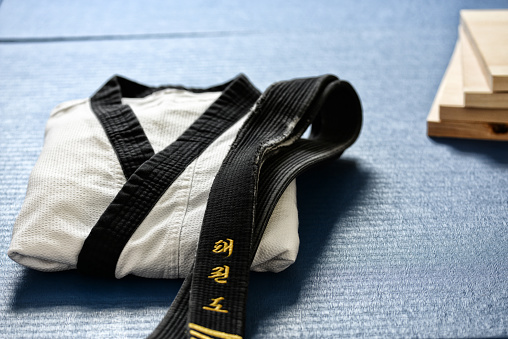 Taekwondo blackbelt, wood boards, and uniform on the floor of a dojang (\