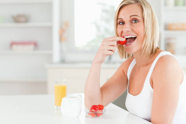istock Young woman sitting at table eats strawberries 825015378