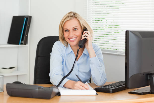 istock Cute businesswoman on phone writing something down looks into camera 825019630
