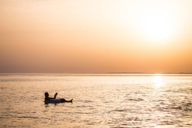 istock Young man in relax in the ocean water on inflatable ring on sunset read a book. 825063558