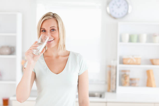 istock Charming woman drinking water while standing looks into camera 825063794