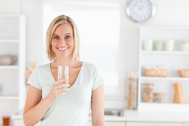 istock Charming woman holding glass filled with water while standing looking into the camera 825063806