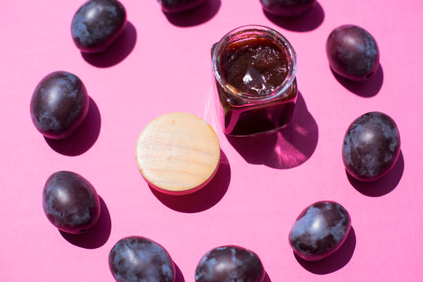 Plum jam in glass jar with ripe plums scattered around. Making preserves at home.