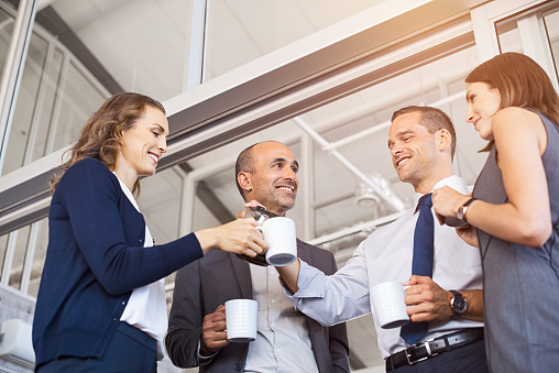 Happy businessman pouring coffee to his colleagues in meeting room. Smiling group of businessmen and businesswoman relax after conference. Low angle view of formal business team take a coffe break after work.