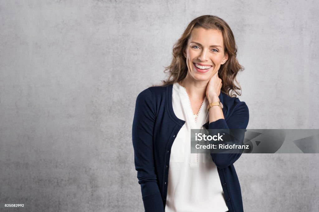 Happy laughing woman Cheerful mid adult woman laughing and looking at camera. Portrait of smiling businesswoman enjoying standing against grey wall. Happy mature woman looking at camera with toothy smile, copyspace. Women Stock Photo