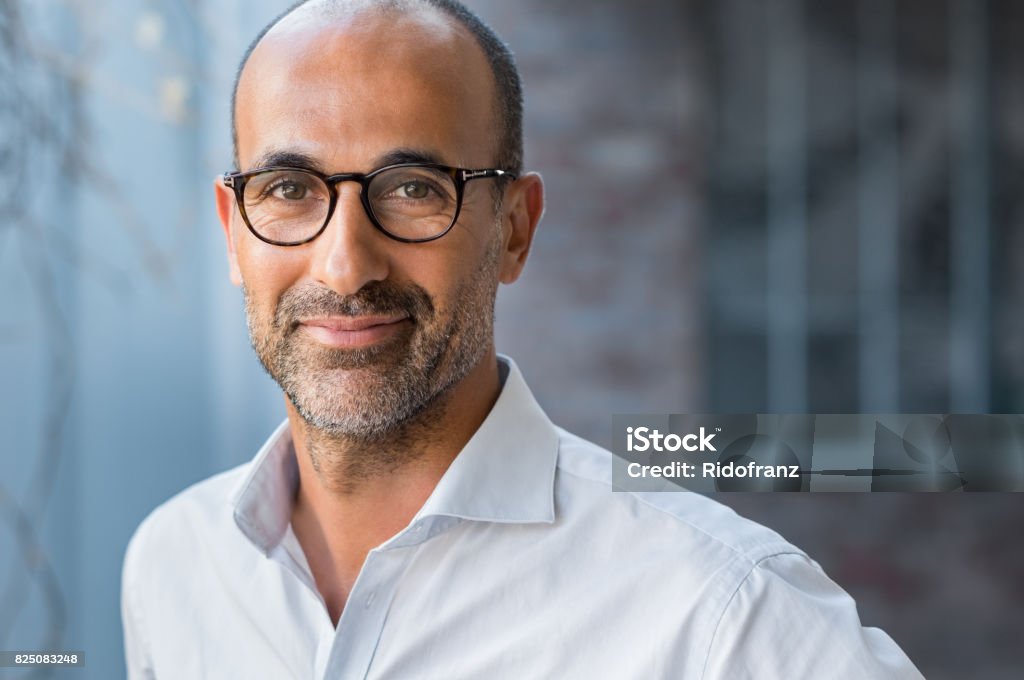 Mature mixed race man smiling Portrait of happy mature man wearing spectacles and looking at camera outdoor. Man with beard and glasses feeling confident. Close up face of hispanic business man smiling. Portrait Stock Photo