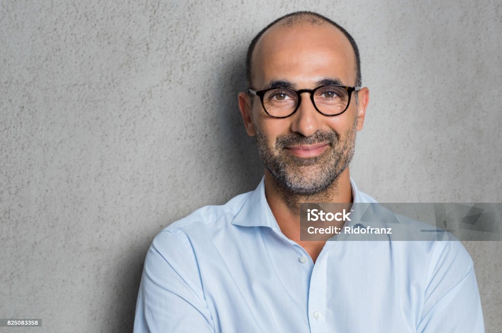 Businessman wearing eyeglasses Portrait of a mature businessman wearing glasses on grey background. Happy senior latin man looking at camera isolated over grey wall with copy space. Close up face of happy successful business man. Portrait Stock Photo