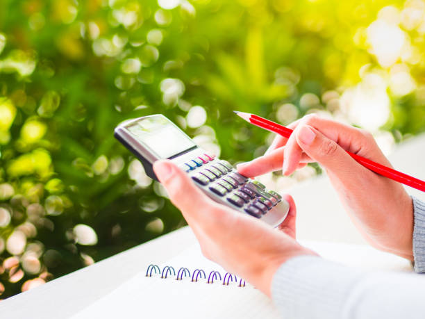 istock woman hand working with calculator and holding red pencil, business document and note book on working table with nature green leaves background. 825086452