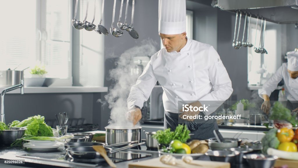 Berühmten Koch ein großes Restaurant bietet Gerichte mit seiner Hilfe der Köche. Moderne Küche ist der Edelstahl gemacht und voll von kochen Zutaten. - Lizenzfrei Arbeitskollege Stock-Foto