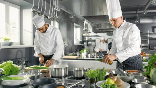 istock Two Famous Chefs Work as a Team in a Big Restaurant Kitchen. Vegetables and Ingredients are Everywhere, Kitchen Looks Modern with Lots of Stainless Steel. 825096040