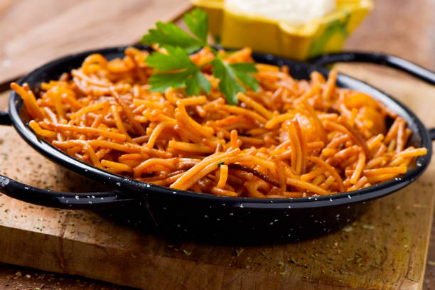 closeup of a spanish fideua, a typical noodles casserole with seafood, in a paella pan and aioli sauce in a yellow mortar on a rustic wooden table