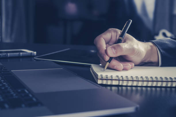 istock Businessman writing idea on paper notebook with laptop computer on working desk 825109250