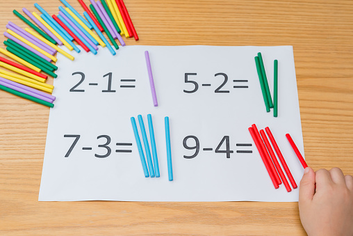kid learning simple subtraction by counting numbers of sticks