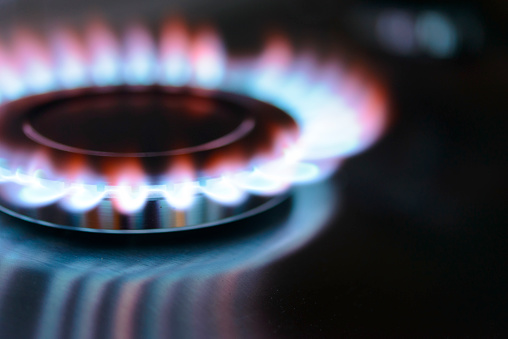 Blue and orange flames on a gas stove burner with a dark background.