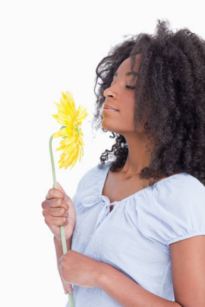 Young curly woman smelling a beautiful flower against a white background