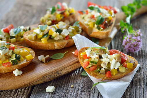 Warm vegetarian canapes: Baked crostini with mixed Greek vegetables with feta cheese served on a wooden cutting board