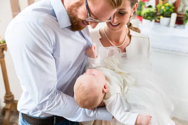 Young parents at the church with their baby wearing a christening gown