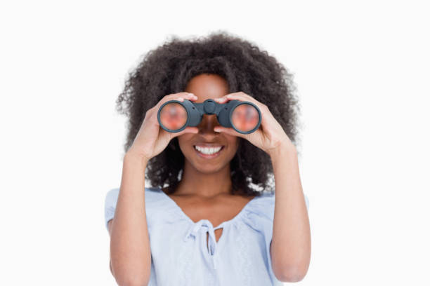 Young woman with curly hair looking through binoculars Young woman with curly hair looking through binoculars against a white background searching binoculars stock pictures, royalty-free photos & images