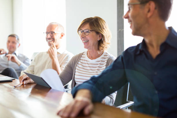 Business people during meeting in board room Smiling female entrepreneur in meeting with colleagues at startup office. Business people smiling during meeting in board room. middle age adult studying stock pictures, royalty-free photos & images