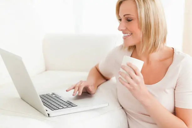 Close up of awoman holding a mug while using a notebook in her living room