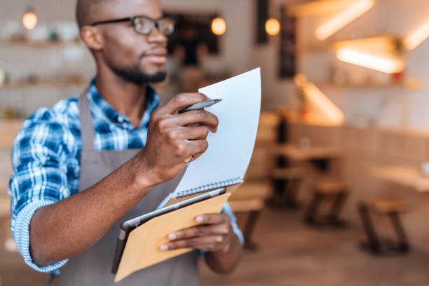 istock handsome african american waiter taking order with notepad and digital tablet in cafe, selective focus 825191620
