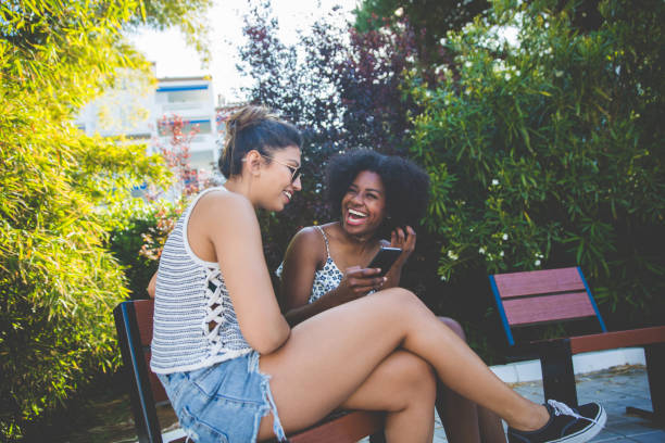 istock Two young happy girls sitting outside using mobile laughing 825198118