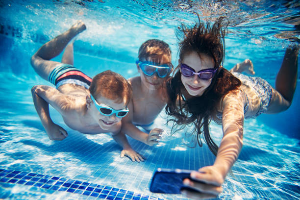 Three happy kids taking selfies underwater Brothers and sister are having fun playing underwater in the resort pool.  Kids are taking selfies using waterproof smartphone.
 waterproof photos stock pictures, royalty-free photos & images