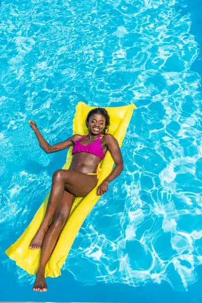 Photo of African american woman floating on inflatable mattress in swimming pool