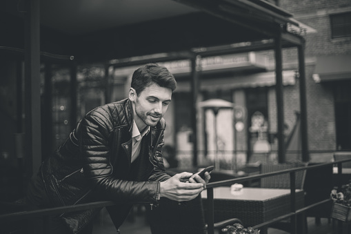 Young handsome looking businessman in biker jacket, standing at the cafe, waiting for a friend.