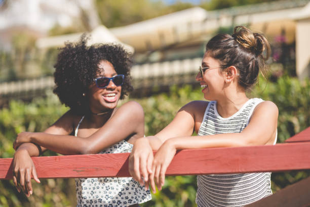 istock Two female friends leaning against fence talking 825203810