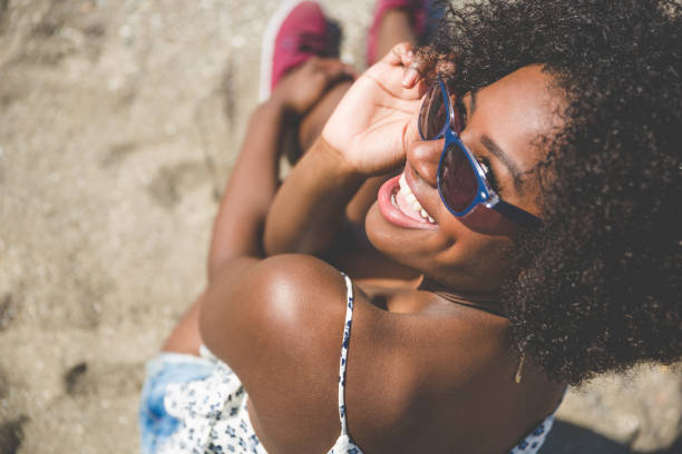istock Young afro american girl sitting on sand laughing 825203890