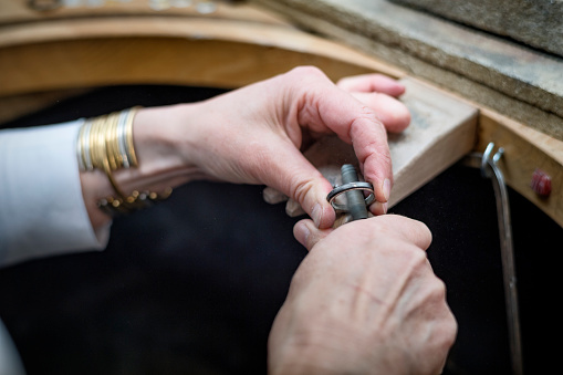 Close up of a Goldsmith’s hands at work creating a silver ring in her workshop. Colour, horizontal with some copy space.