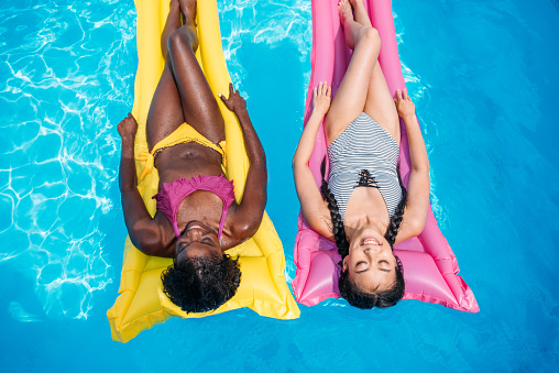 Young multiethnic women floating on inflatable mattresses in swimming pool at resort