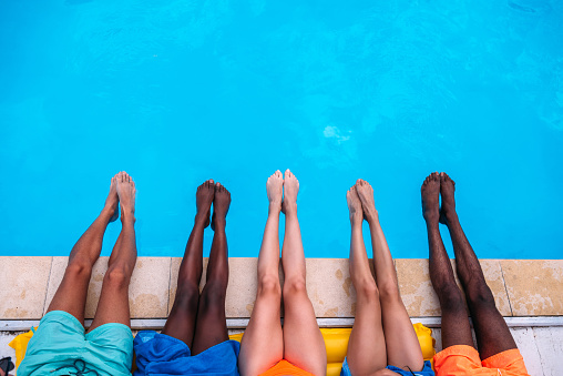 Young people lying near swimming pool. Cropped image of legs over blue water