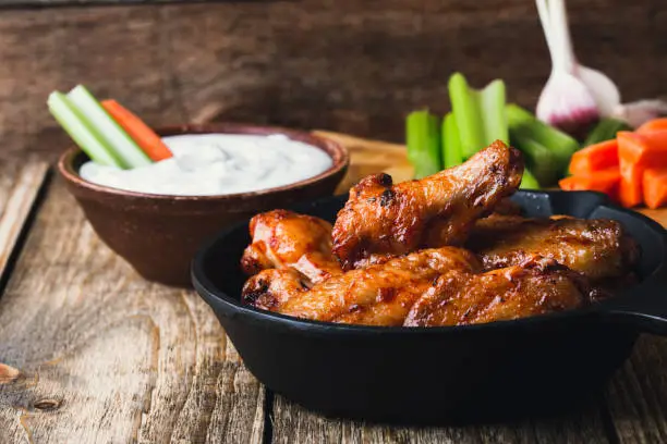 Roasted chicken wings with carrots, celery sticks and dipping sauce on rustic wooden table