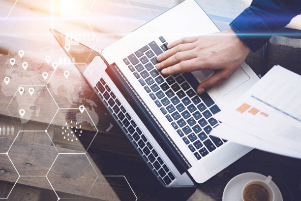 istock Concept of digital screen,geolocation icon,virtual diagram,graph interfaces.Man working with laptop at office at wooden table.Reflections on glass surface.Horizontal closeup,flares. 825223686