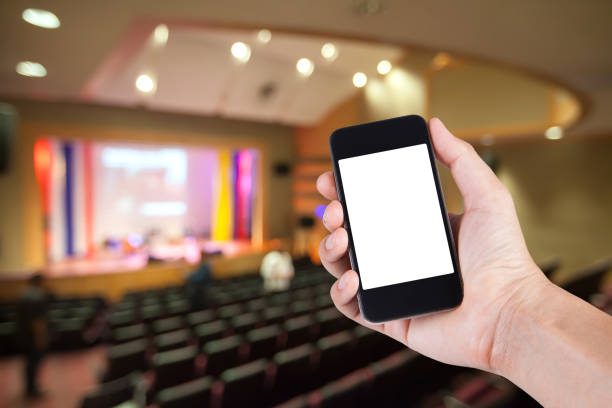 istock Smartphone on hand and white screen with blurry background of theater. 825224230
