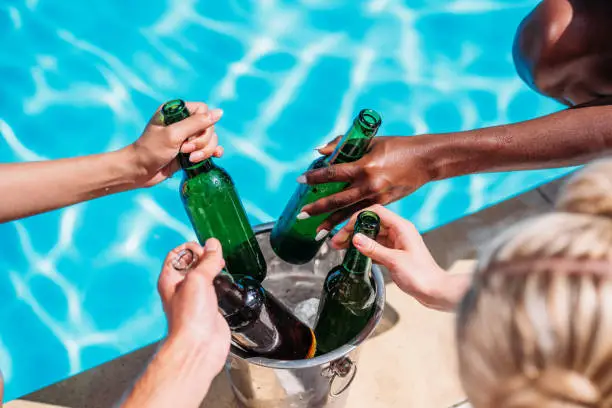 Photo of Cropped image of human hands taking cold beer from Ice bucket standing on edge of swimming pool
