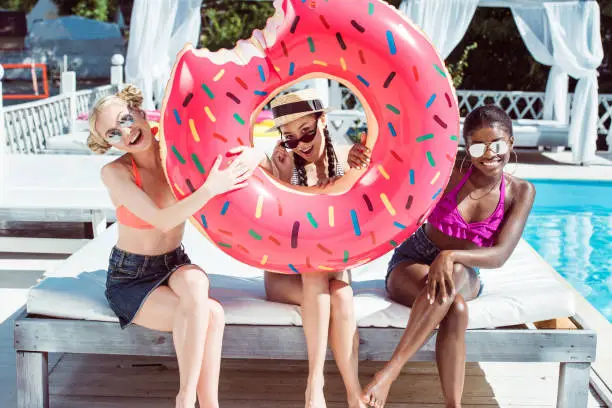Photo of Happy multiethnic women posing with inflatable donut near swimming pool at resort
