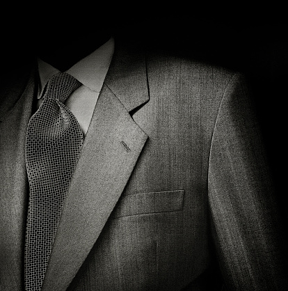 Black & White film photo of man suit detail against black background. Low key exposure to give it a sinister semblance.