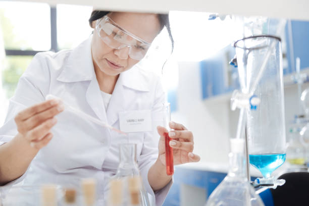 istock Nice smart woman putting chemical reagent into a flask 825250312