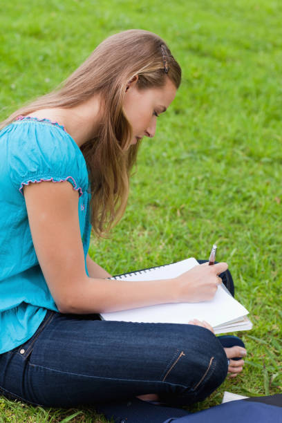 istock Serious young girl writing on her notebook while sitting on the grass 825254254