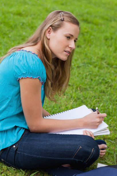 istock Attractive young girl sitting down in a park while doing her homework 825254302
