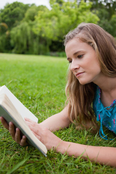 istock Young woman reading a book while lying on the grass 825255304