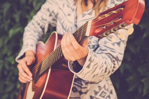 Close up of stylish female playing acoustic guitar in nature. Fashion and music concepts.